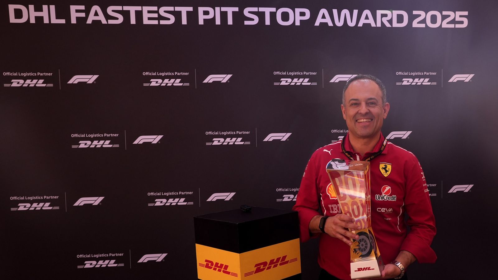 This image shows a Ferrari team member holding the trophy for the 2025 DHL Fastest Pit Stop Award